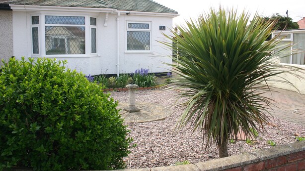 Une maison blanche avec un toit en tuiles, un pilier en pierre et un grand yucca dans le jardin.