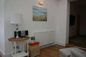 Une pièce avec une lampe blanche, un tableau représentant un phare, un radiateur, un téléviseur et un panier en osier.