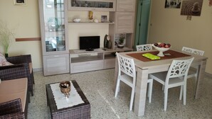 A dining area with a table set for four, a television on a cabinet, and a green door in the background.
