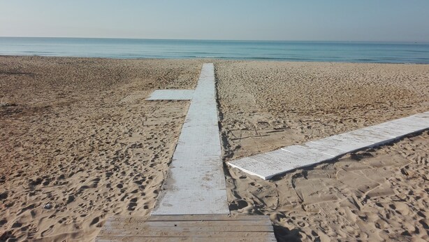 A beach with a wooden walkway leading to the sea.