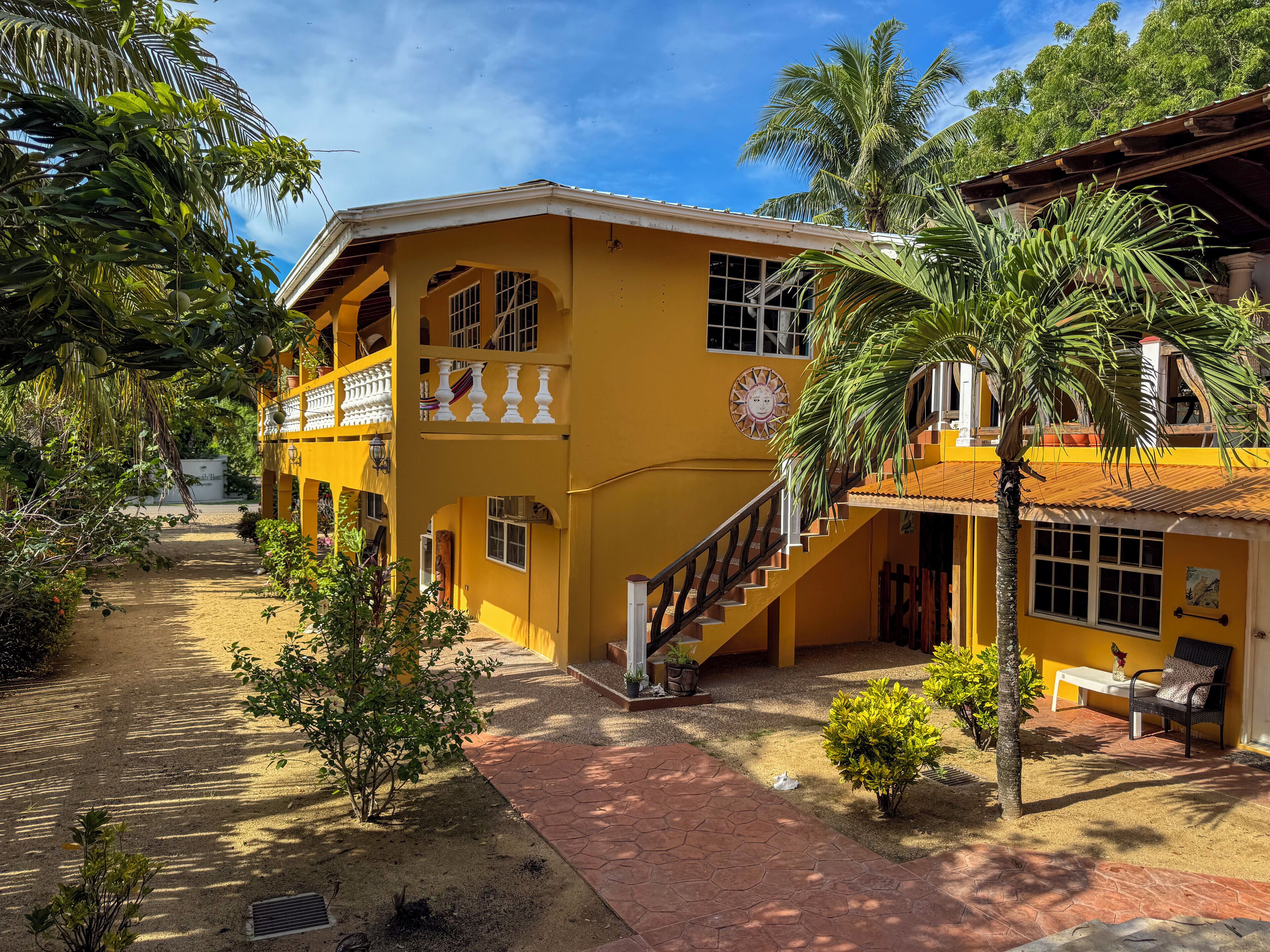 A yellow building with a staircase, a balcony, and a palm tree.