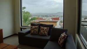 A living room with a large window, a dark sofa, and patterned cushions. - The Best Vacation Place in the Heart of Ensenada with Panoramic view (Ensenada)