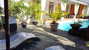 Zona junto a la piscina con sillas de descanso, plantas en macetas y una piscina.
