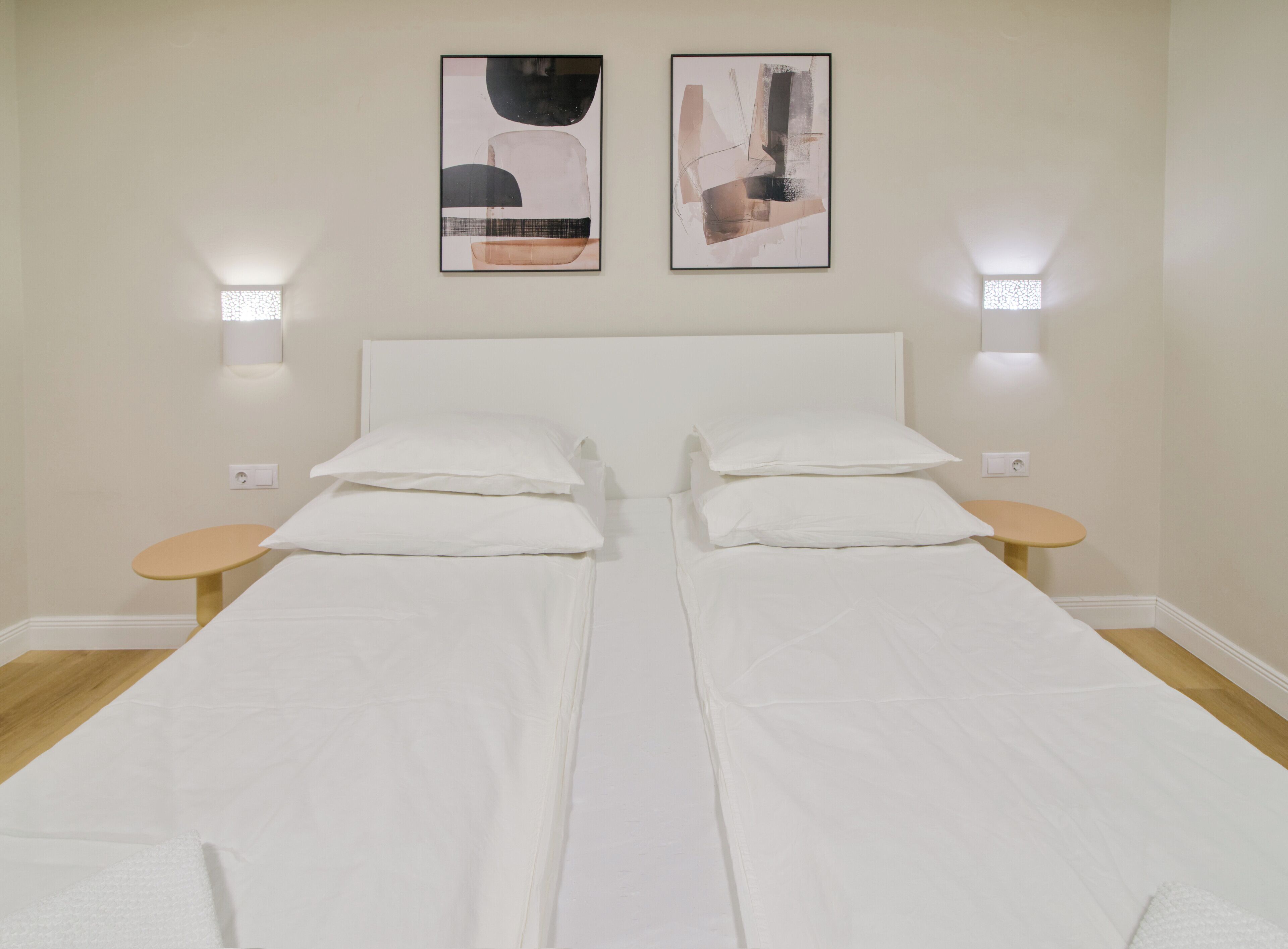 A double bed with white linens, two bedside tables, and two wall-mounted light fixtures.