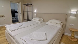 Een tweepersoonsbed met witte lakens en kussens, een nachtkastje en een kleine ronde tafel met een lamp.