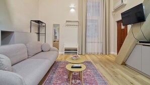 Een moderne woonkamer met een bank, een klein rond tafeltje, een spiegel en een aan de muur bevestigde televisie.