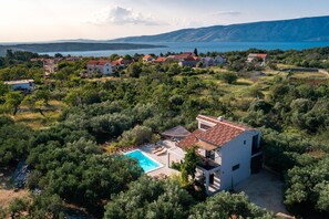 A villa with a swimming pool surrounded by lush greenery and a view of the sea.