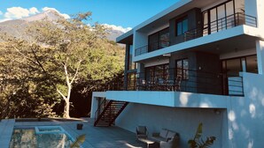 A modern two-story building with a pool, outdoor seating, and a mountain view.