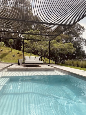 A swimming pool with a covered seating area and surrounding greenery. - Modern paradise at the golf resort (Alotenango)