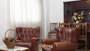 Una sala de estar con un sofá de cuero marrón, una mesa de comedor de madera y una zona de cocina con armarios y un jarrón de flores.