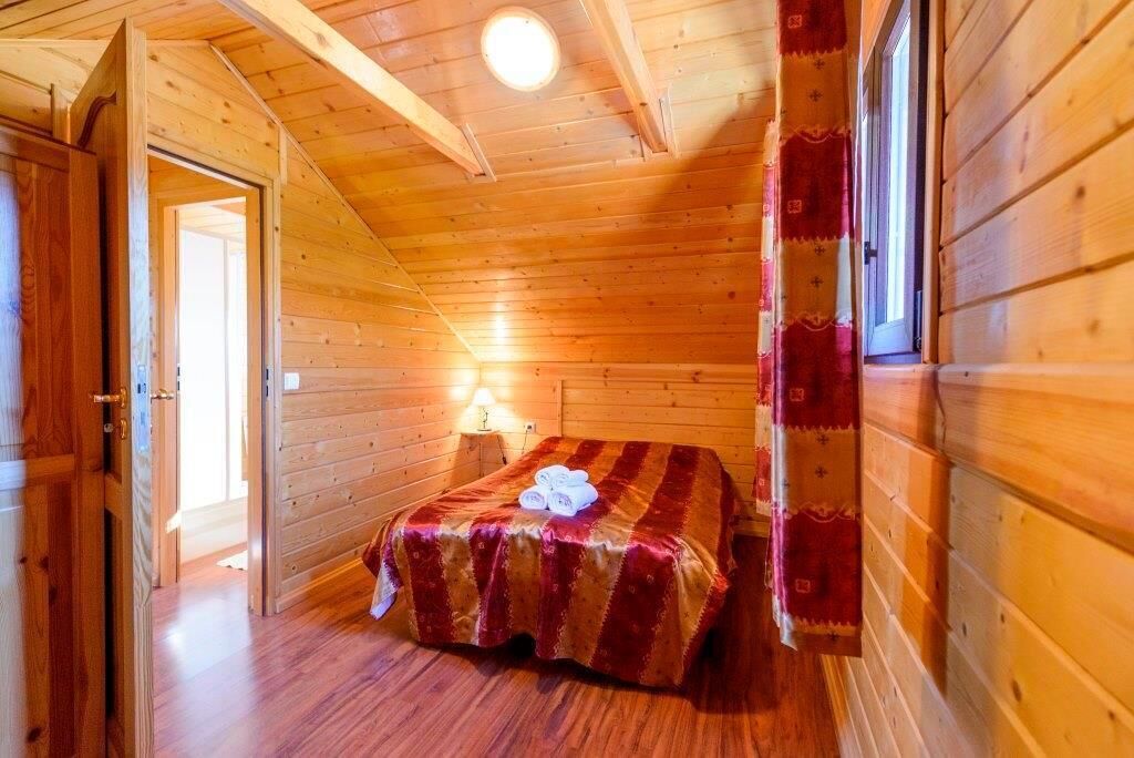 A wooden cabin room with a bed, a nightstand, and a window.