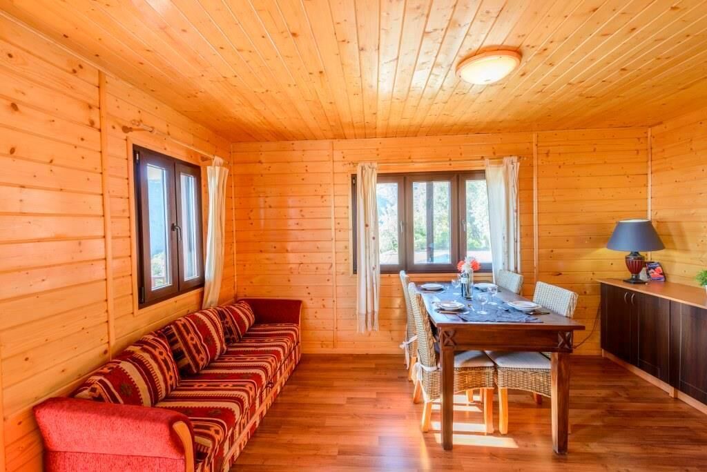 A wooden cabin interior with a sofa, dining table, chairs, and a cabinet.