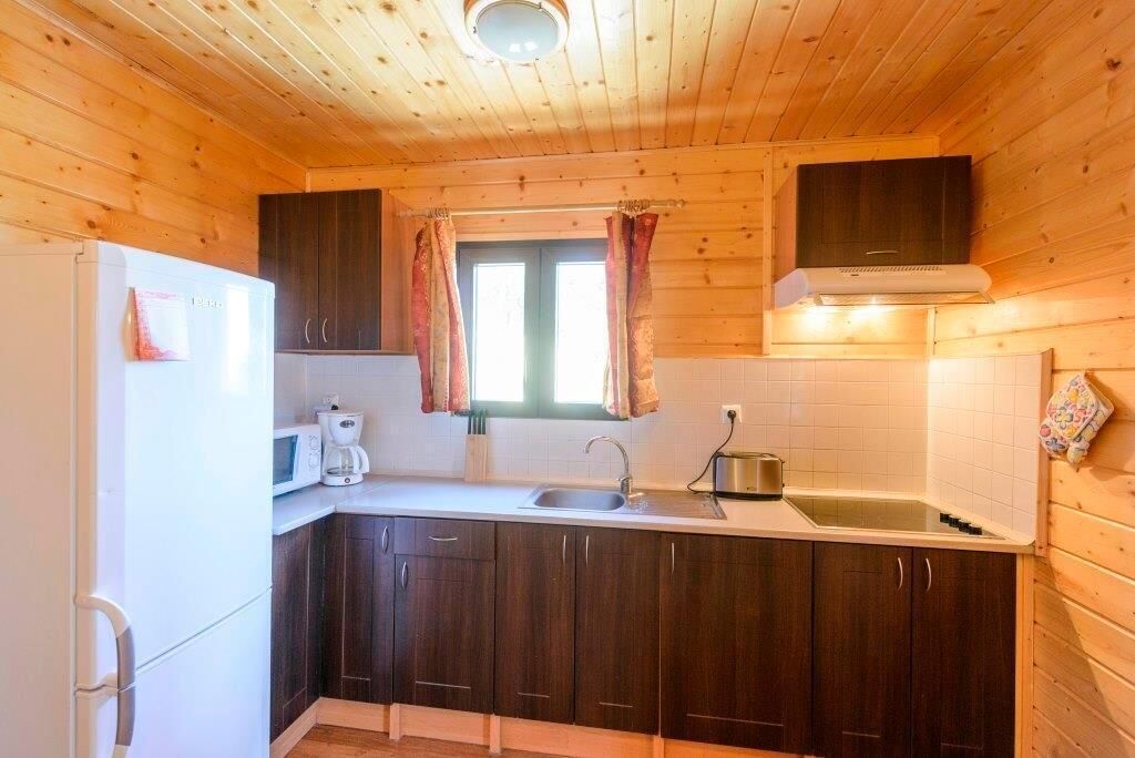 Une cuisine de taille réduite, avec des meubles de rangement en bois, un réfrigérateur blanc, un four à micro-ondes, un évier et une fenêtre agrémentée de rideaux.