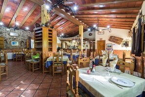 A rustic dining area with wooden tables and chairs, stone walls, and exposed wooden beams.