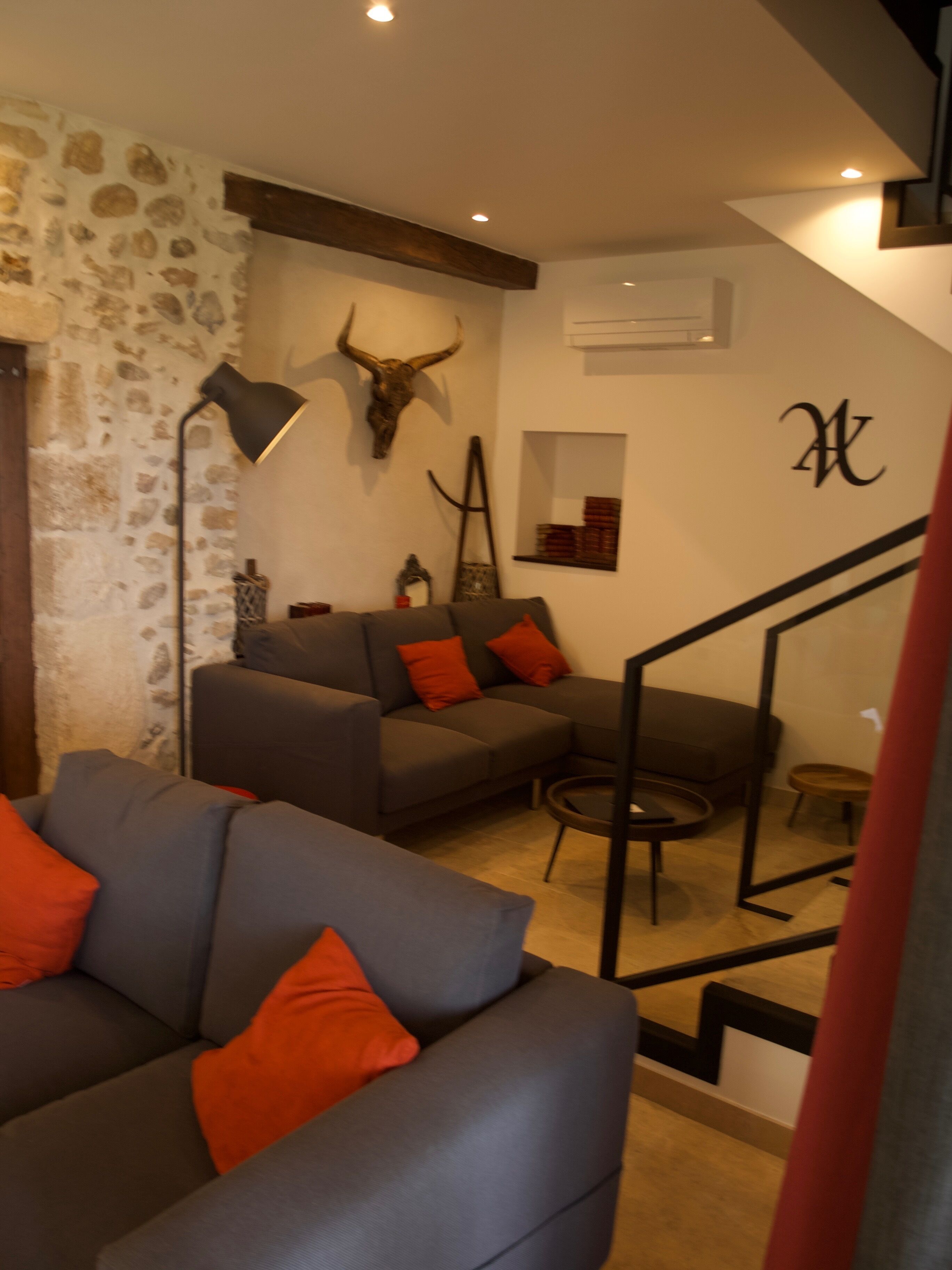 A living room with a stone wall, a sofa with orange cushions, a lamp, and a bull's head mounted on the wall.