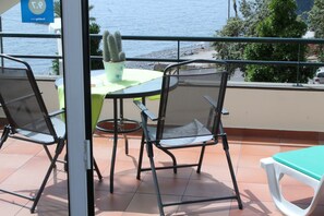 Enjoy the ocean view from this balcony with a table, two chairs, and a potted cactus.