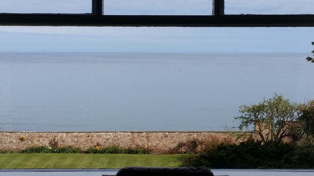 A view through a window of a room with a stone wall and a grassy area in front. - Sea View Apartment with commanding sea views in Crail (Crail)