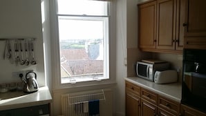 A kitchen with wooden cabinets, a microwave, a toaster, and a kettle on the counter. - Sea View Apartment with commanding sea views in Crail (Crail)