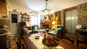 Un salon chaleureux avec une table à manger dressée pour le repas, entouré de murs en pierre et agrémenté d’une cheminée.