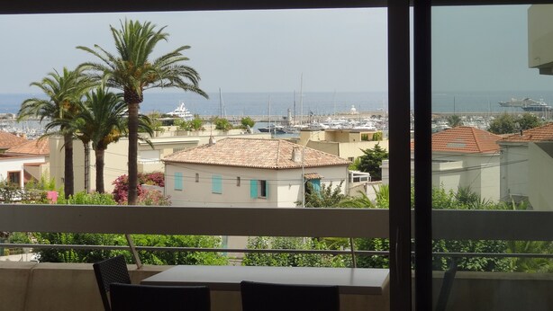 A balcony with a table and chairs, overlooking a marina with boats and a coastal town. - Seaview Apartment with a lovely harbour view, terrace and parking (Antibes)