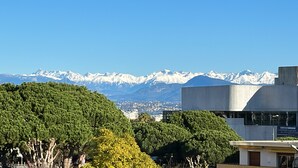 A modern building with a view of snow-capped mountains in the background. - Seaview Apartment with a lovely harbour view, terrace and parking (Antibes)