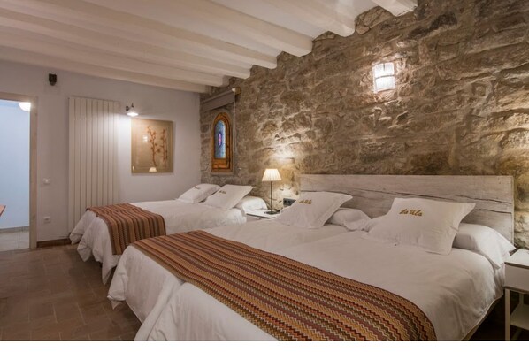 A bedroom with two beds, a stone wall, a stained glass window, and a door.