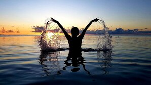 Silueta di una persona con le braccia alzate nell'acqua al tramonto.