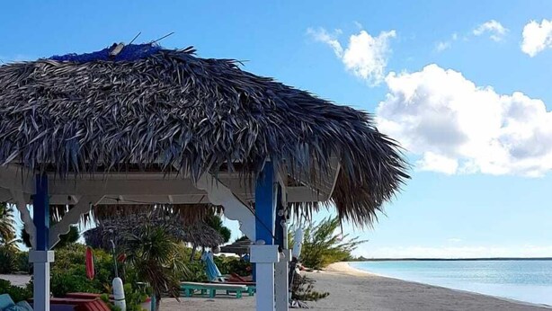 Un’area relax in spiaggia con tetto di paglia, poltroncine e vista sull'oceano.