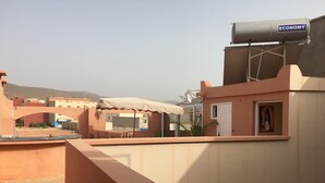 Una terraza en la azotea con un tanque de agua marcado 'ECONOMY', una zona de estar cubierta y vistas de edificios circundantes.
