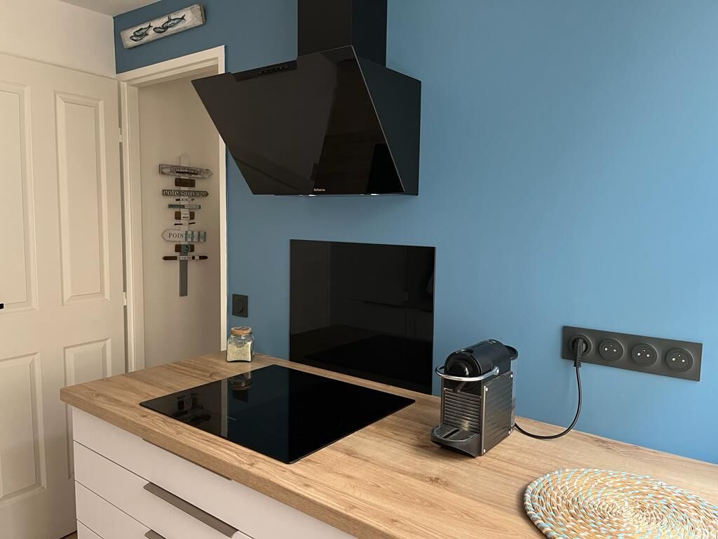 Une cuisine équipée d’une plaque de cuisson à induction noire, d’une machine à café et d’une prise électrique murale.