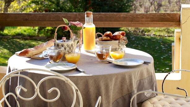 A round table with a tablecloth, a bottle, glasses, and food items.