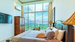 A bedroom with a large window, a bed, a wardrobe, a television, and a lamp. - 24o Penthouse Unique Design 2 Balconies Oceanview (Panama City)