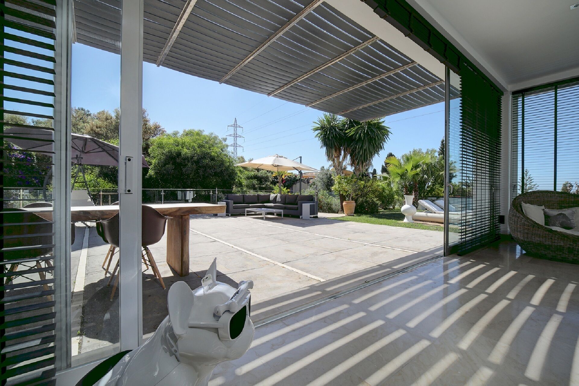 A modern outdoor patio area with a covered seating area, a dining table, and a decorative sculpture.