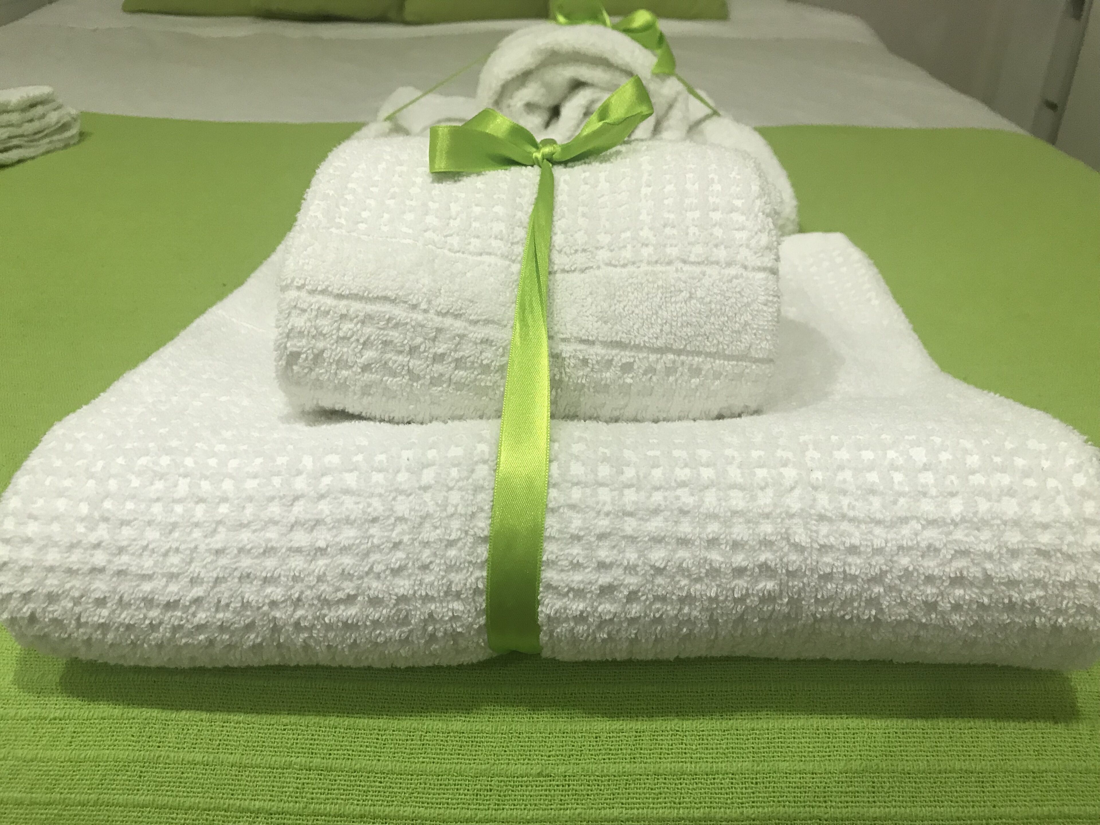 A neatly folded white towel with a green ribbon tied around it, placed on a green textured surface.