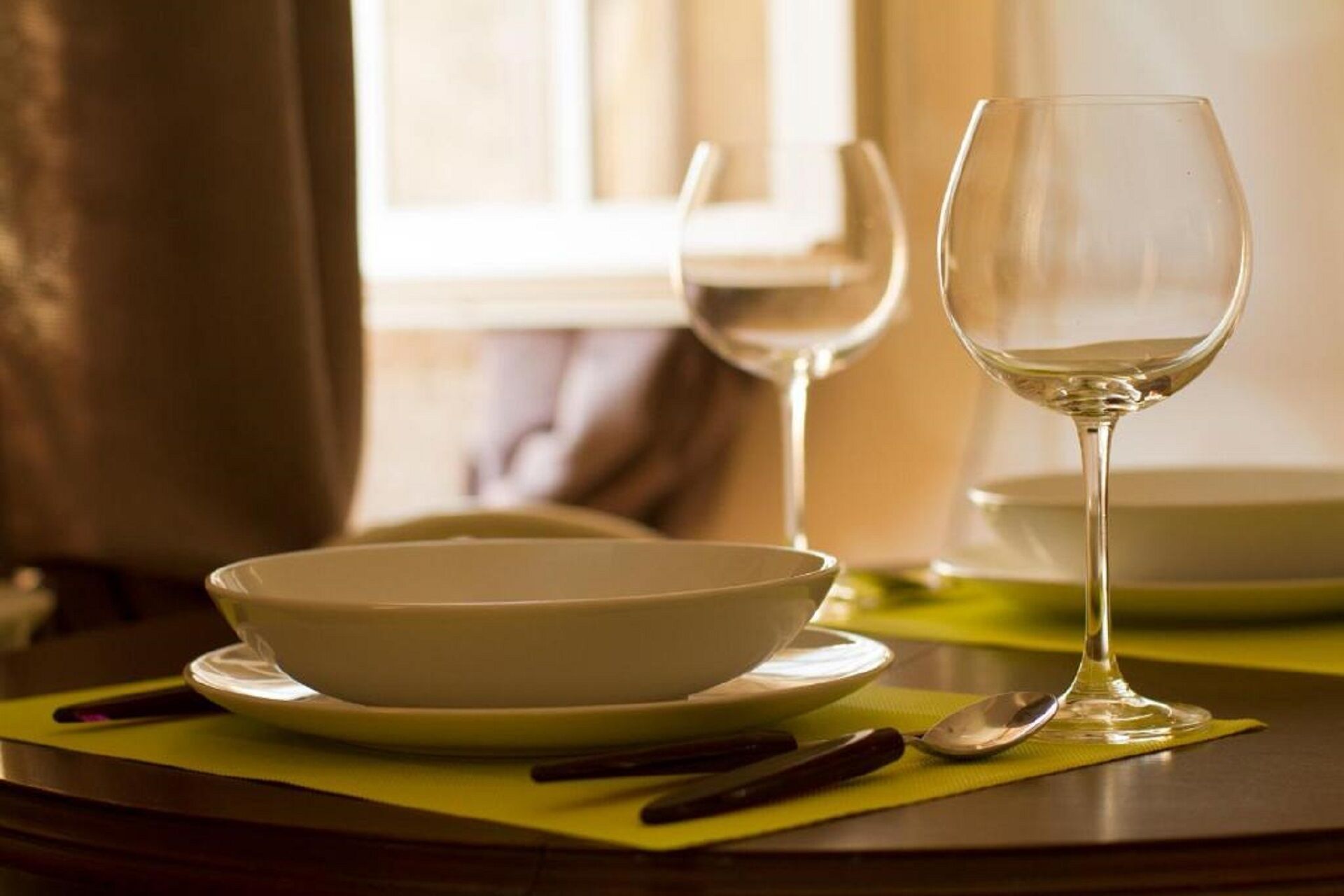 A dining table with a bowl, a wine glass, and cutlery.