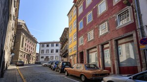 A narrow cobblestone street lined with colorful buildings, parked cars, and a clear blue sky. - Home4you Downtown Porto (Porto)