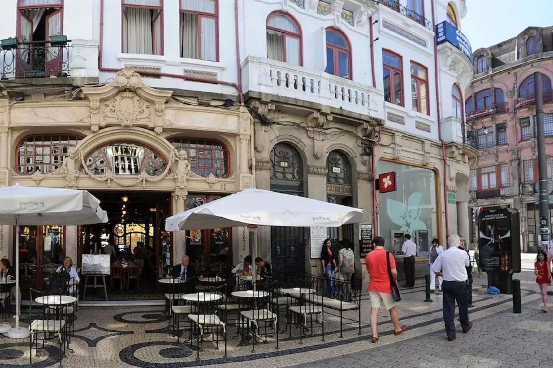 An outdoor café with tables and chairs, a building with ornate architecture, and a street with pedestrians.