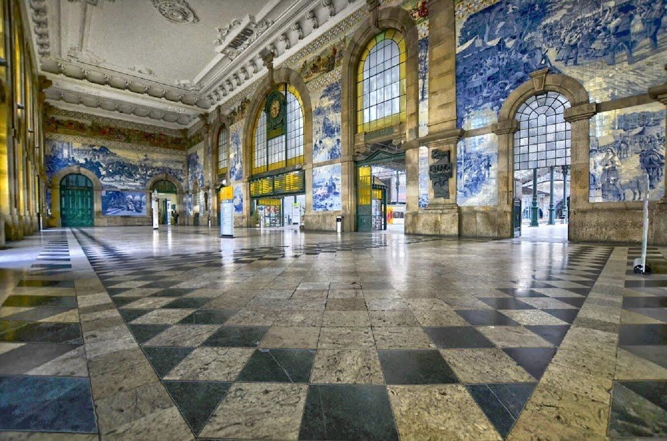 Ein geräumiger Saal mit Schachbrettmuster-Boden, großen Bogenfenstern und aufwendigen Wandmalereien.