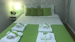 A neatly made bed with green bedding and pillows, a bedside table with a lamp and a plant, and three towels with green ribbons. - Home4you Downtown Porto (Porto)