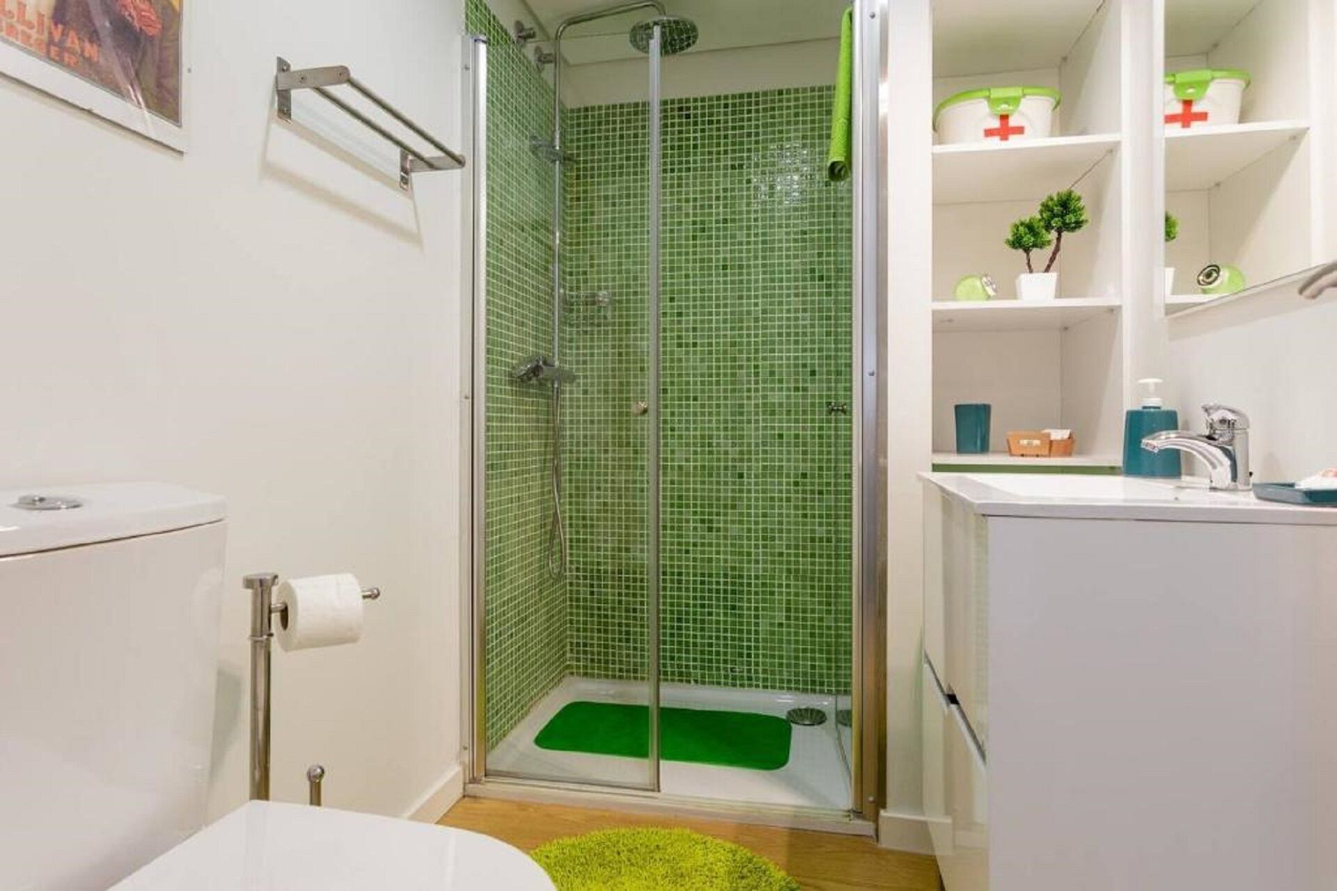 Une salle de bain équipée d’une douche, de toilettes, d’un lavabo et dont l’espace douche est carrelé de carreaux verts.