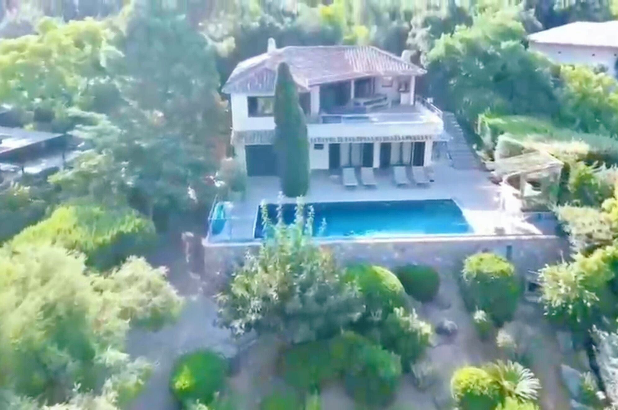 A large house with a swimming pool surrounded by lush greenery.