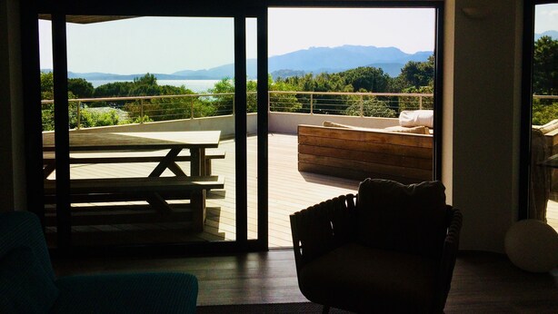 Ein Zimmer mit einer Schiebetür zu einer Terrasse im Freien, mit einem Tisch und einer gepolsterten Sitzecke.