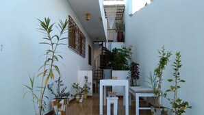 A narrow courtyard with tiled flooring, white walls, and several potted plants. There is a white table and a small bench in the center. - Holiday house 200 meters from Laginha beach (Mindelo)