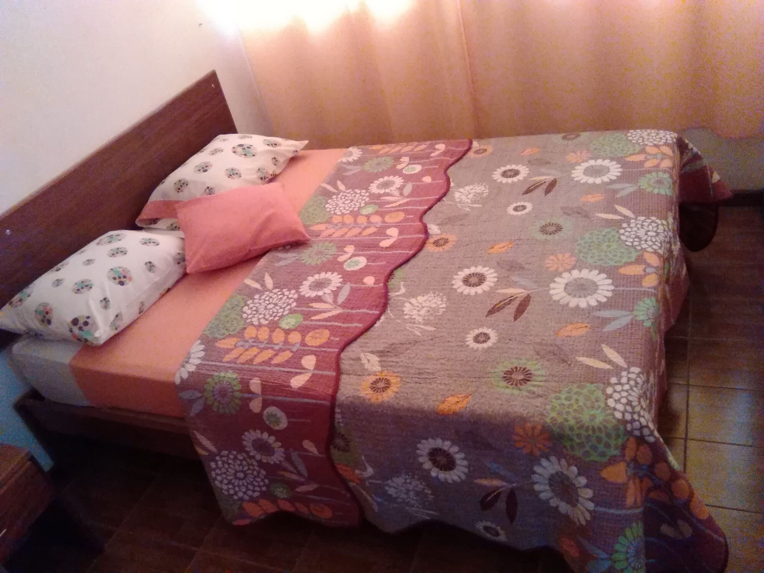 Un lit avec une couvre-lit à motifs floraux, un oreiller rose et un oreiller blanc à motifs.