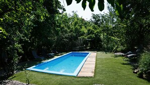 Ein rechteckiger Pool mit Holzterrasse, umgeben von gepflegtem Rasen und üppiger Bepflanzung.
