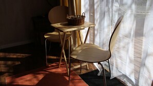 Ein kleiner Holztisch mit einem Korbwäscher, einem Stuhl und einem Fenster mit durchscheinenden Vorhängen.