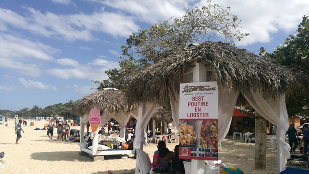 Cena de praia com uma estrutura de telhado de palha anunciando um restaurante de frutos do mar.