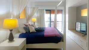 Un dormitorio con una cama, dos lámparas de noche, un televisor y un ventanal con cortinas.