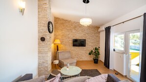 Een woonkamer met een stenen muur, een bank, een salontafel, een televisie en een raam met gordijnen.