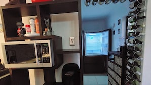 Eine Küche mit Mikrowelle, Toaster und Kaffeemaschine. Ein Regal mit verschiedenen Küchenutensilien und ein wandmontierter Weinkeller.